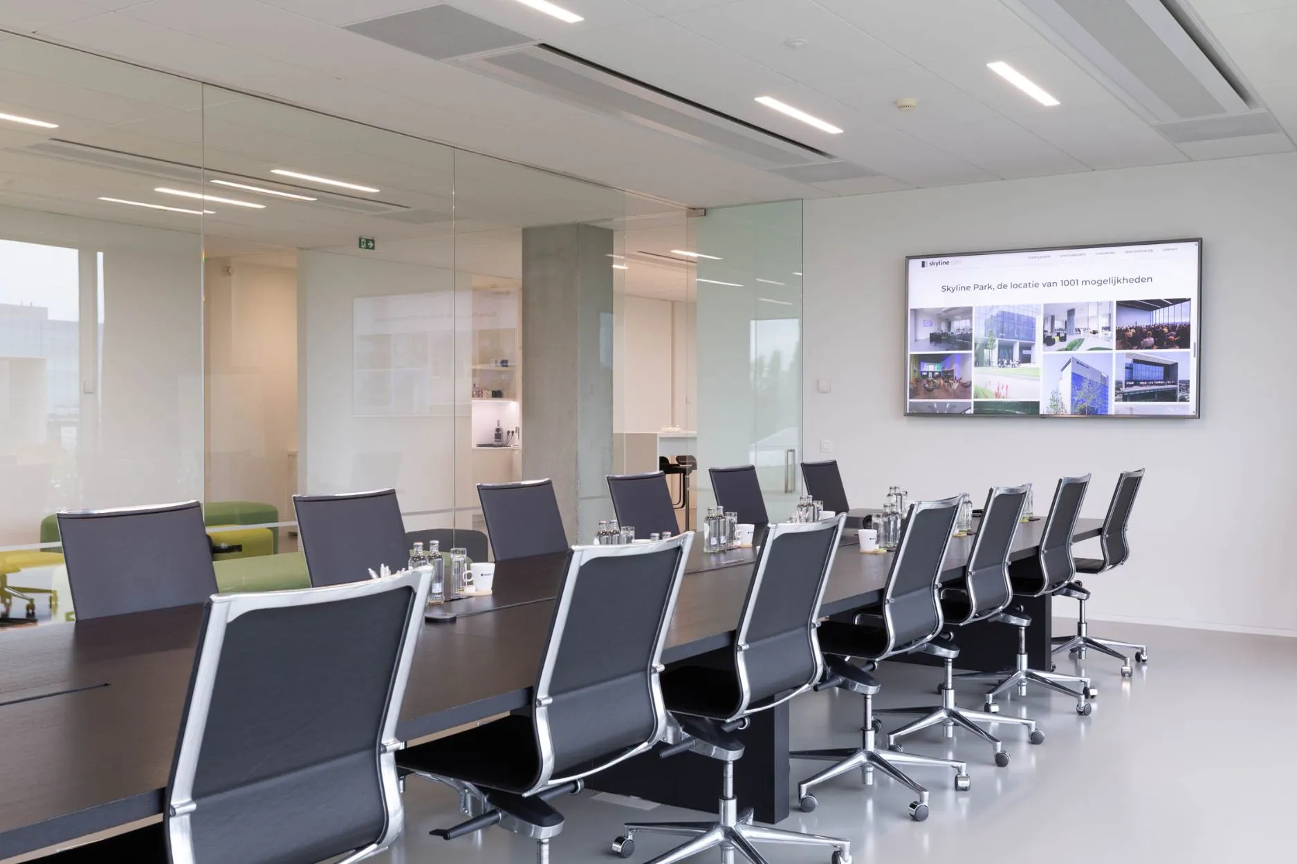 Lichte boardroom met lange vergadertafel, zwarte ergonomische bureaustoelen en presentatiescherm aan de muur, geschikt voor 2 tot 20 personen.