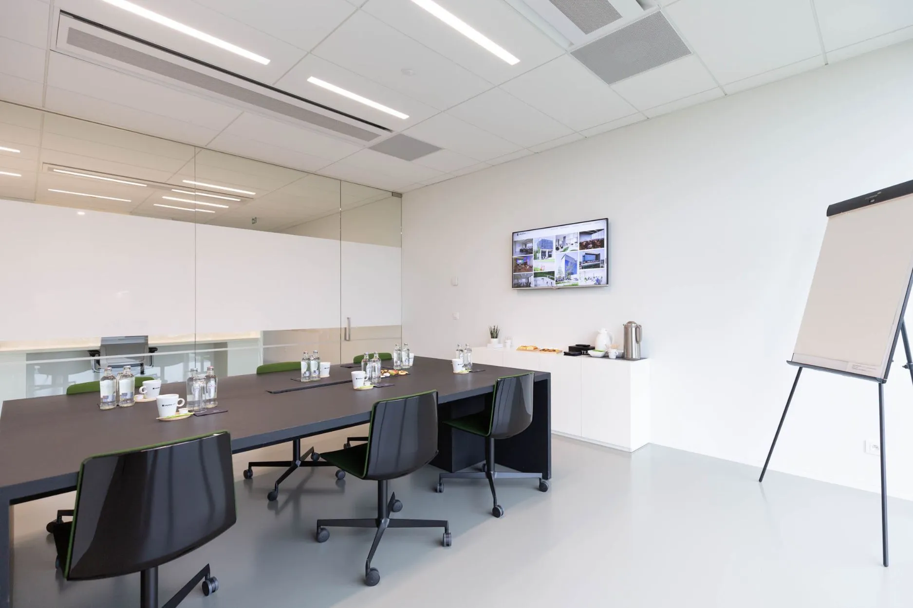 Lichte vergaderzaal 2.01 met donkere tafel, zwarte stoelen, tv-scherm en whiteboard, geschikt voor 2 tot 6 personen.