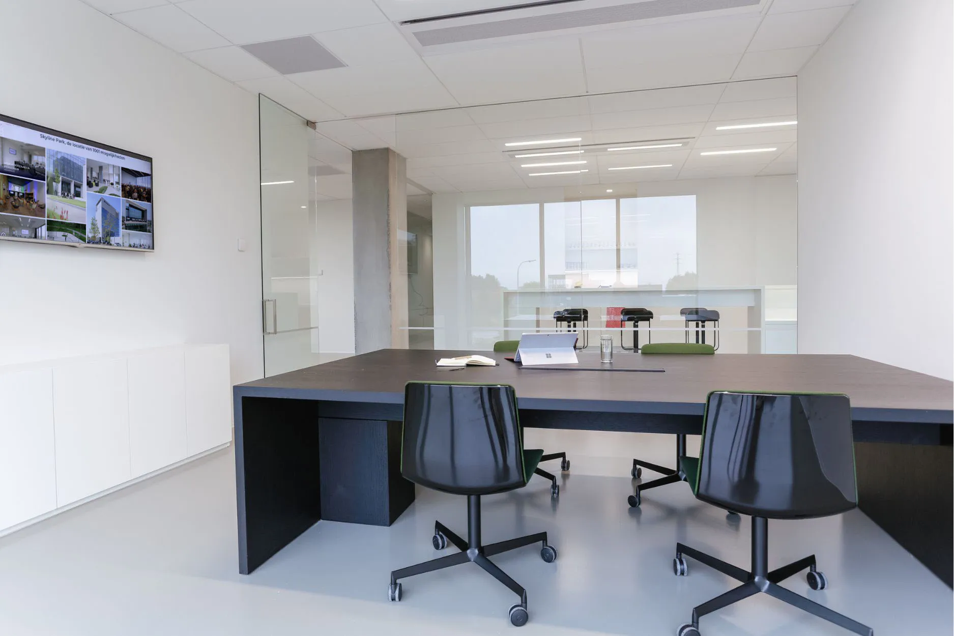 Lichte vergaderzaal 2.02 met donkere tafel, zwarte stoelen, tv-scherm en whiteboard, geschikt voor 2 tot 6 personen.