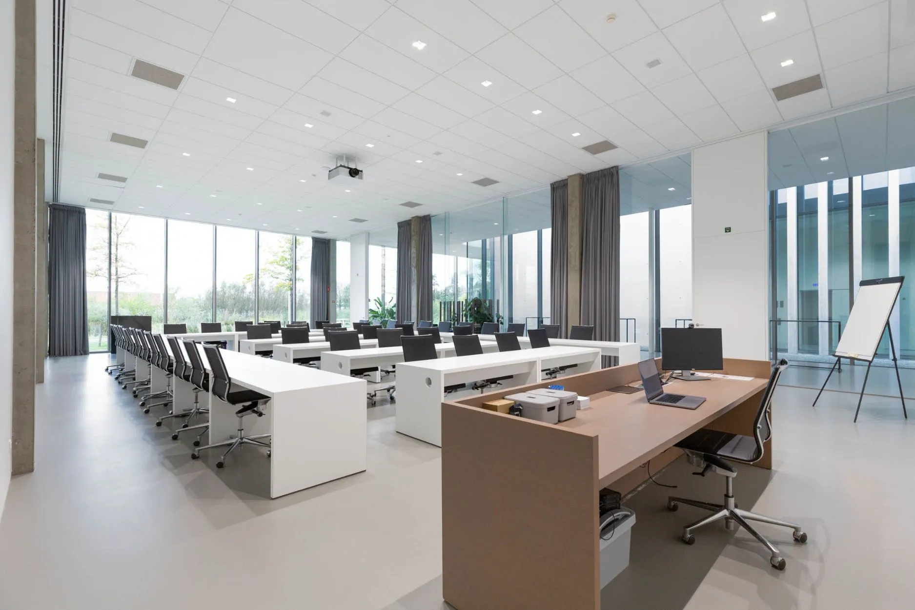 Lichte vergaderzaal met witte tafels in U-opstelling, gekleurde stoelen, plafondbeamer en houten lamellen en gordijnen als scheidingswand