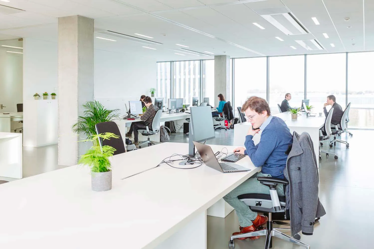 Lichte open coworking space in Skyline Park Izegem met meerdere professionals die werken aan laptops en desktops, omgeven door groene planten.